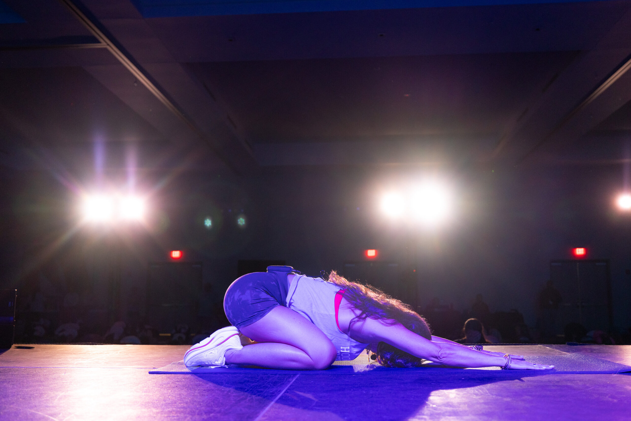 A REV+FLOW participant resting in child's pose on a lit stage