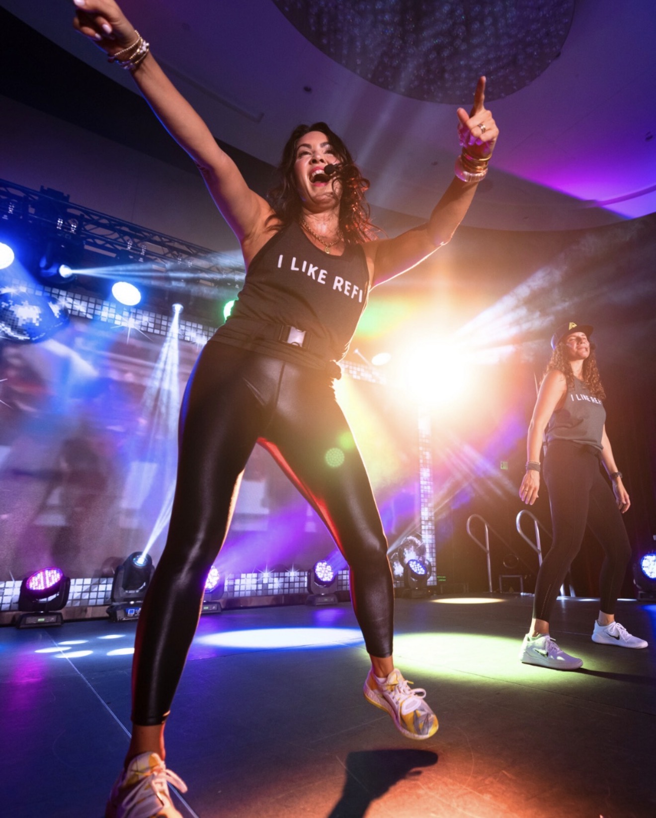 A REFIT Instructor mid-motion on a stage lit in magenta and cyan